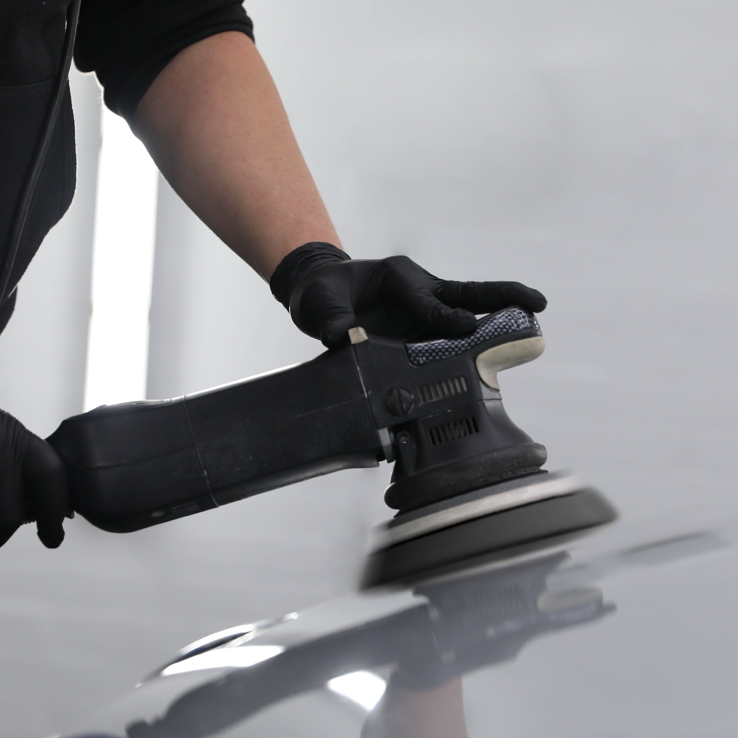 Machine polisher applying fine compound to a car