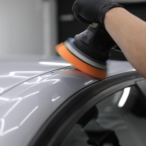 dual action machine polisher applying medium cutting compound to car paintwork